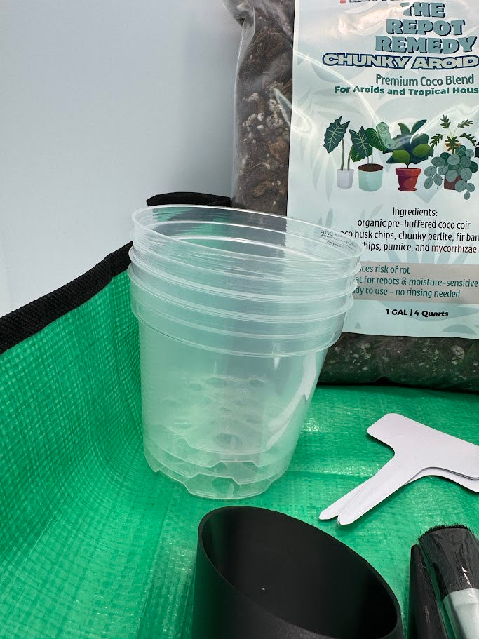 Clear plastic pots, REPOT REMEDY soil mix, and gardening tools on a green mat.