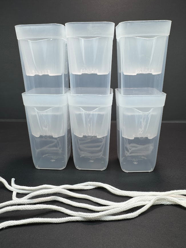 Six translucent white plastic storage containers arranged in two rows of three on a dark gray background, with several white cords or ties laid in front.