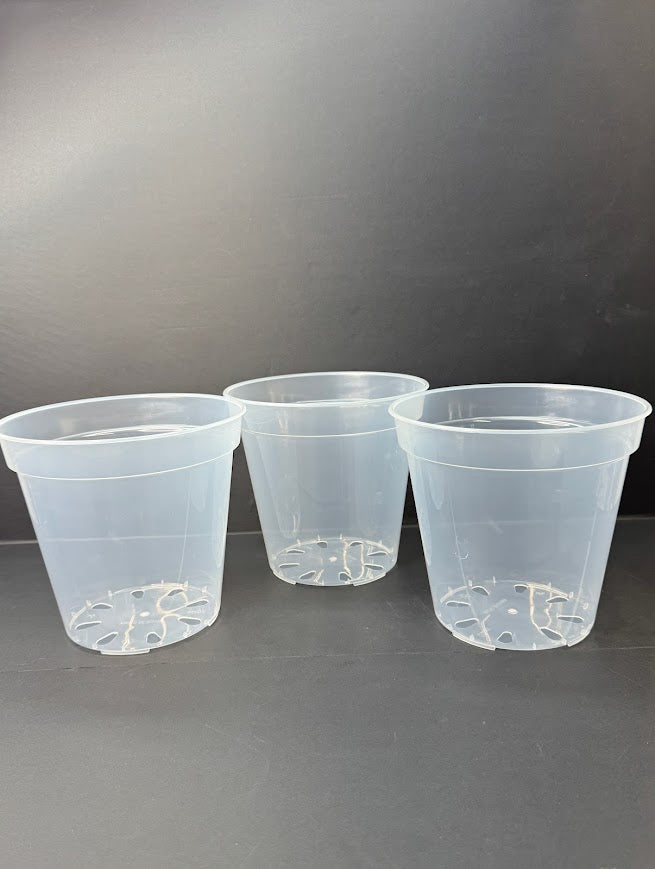 Three clear plastic nursery pots with drainage holes, arranged side-by-side on a dark gray surface against a dark gray background.