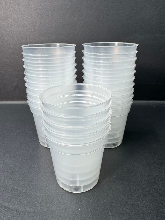 Three stacks of clear plastic cups with a ribbed exterior, arranged on a dark gray surface against a dark gray background.