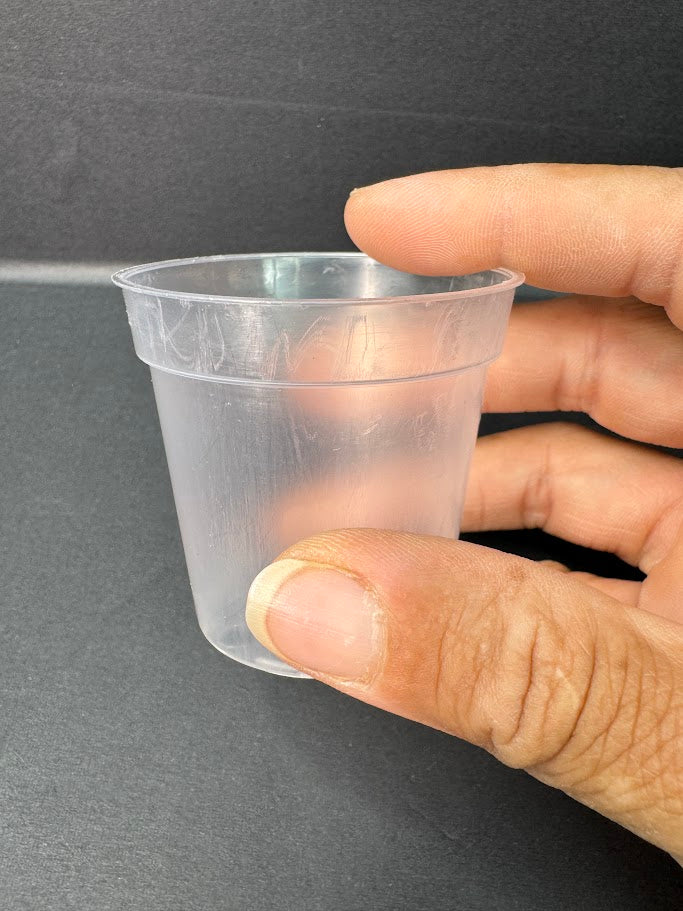 A hand holding a small, clear plastic cup against a dark gray background.
